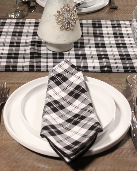 Plaid napkin on a white plate with a checkered placemat and decorative candle in the background.