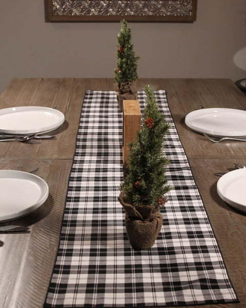 Dining table set with a menzies black and white plaid runner, small Christmas trees, and white plates.