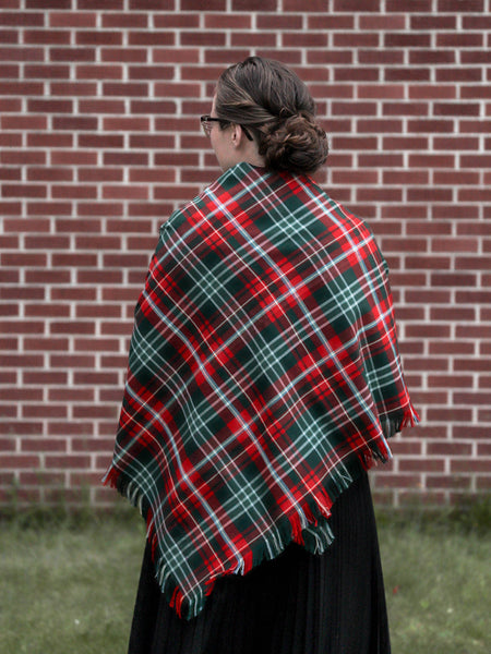 Person wearing a red and green plaid shawl against a brick wall.