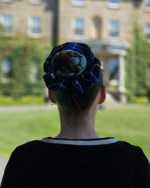 Person wearing a blue patterned scrunchie with a blurred background of a building and greenery