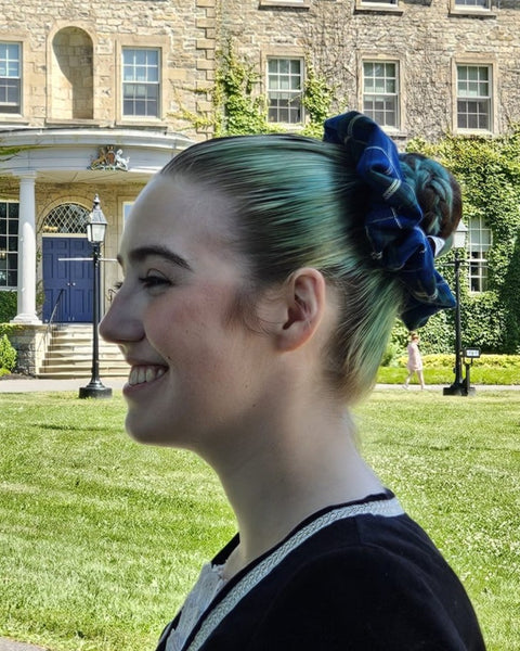 Highland Dancer with green hair and a blue plaid scrunchie in front of a stone building