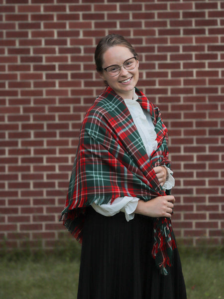 Person wearing a red and green plaid shawl in front of a brick wall