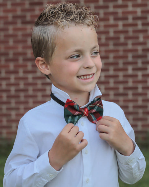 Young boy adjusting a New Brunswick tartan plaid bow tie against a brick wall.
