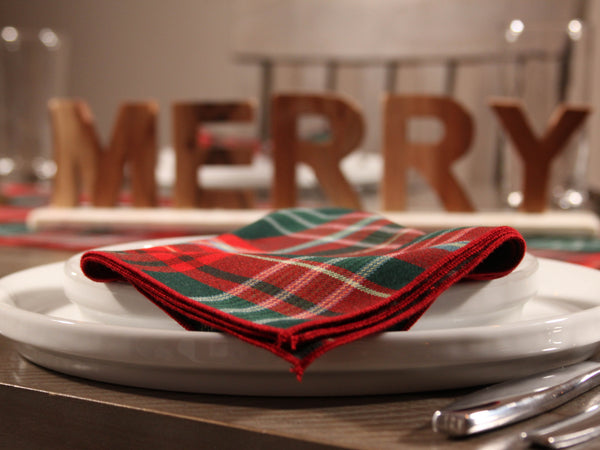 Red and green plaid napkin made by Taylors Tartans on a white plate with 'MERRY' letters in the background