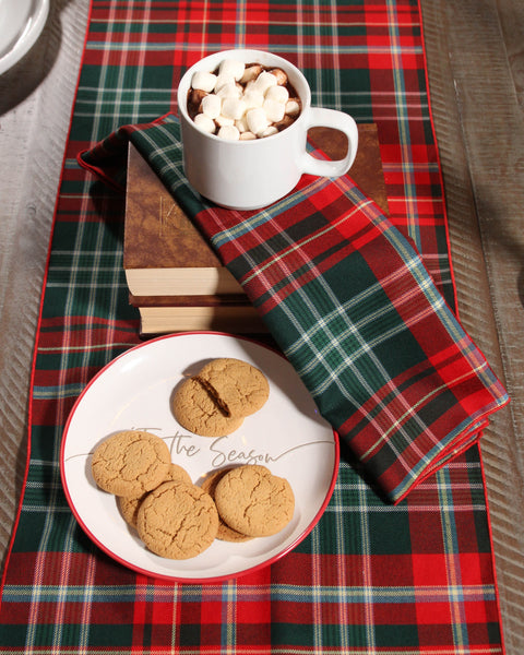 Hot chocolate with marshmallows and cookies on a red and green plaid table runner