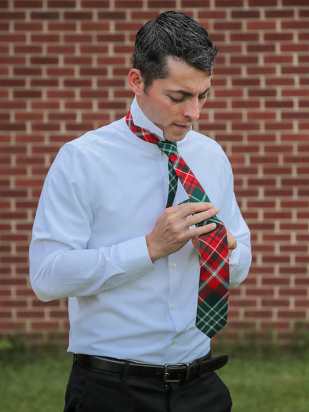 Man adjusting a plaid tie against a brick wall