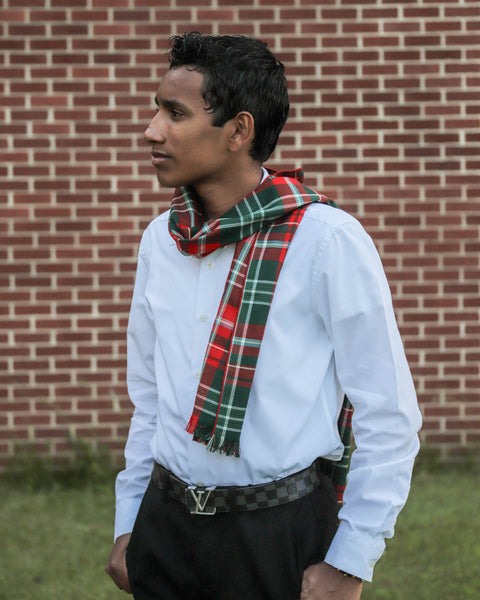 Youth man wearing a white shirt and New Brunswick plaid scarf in front of a brick wall