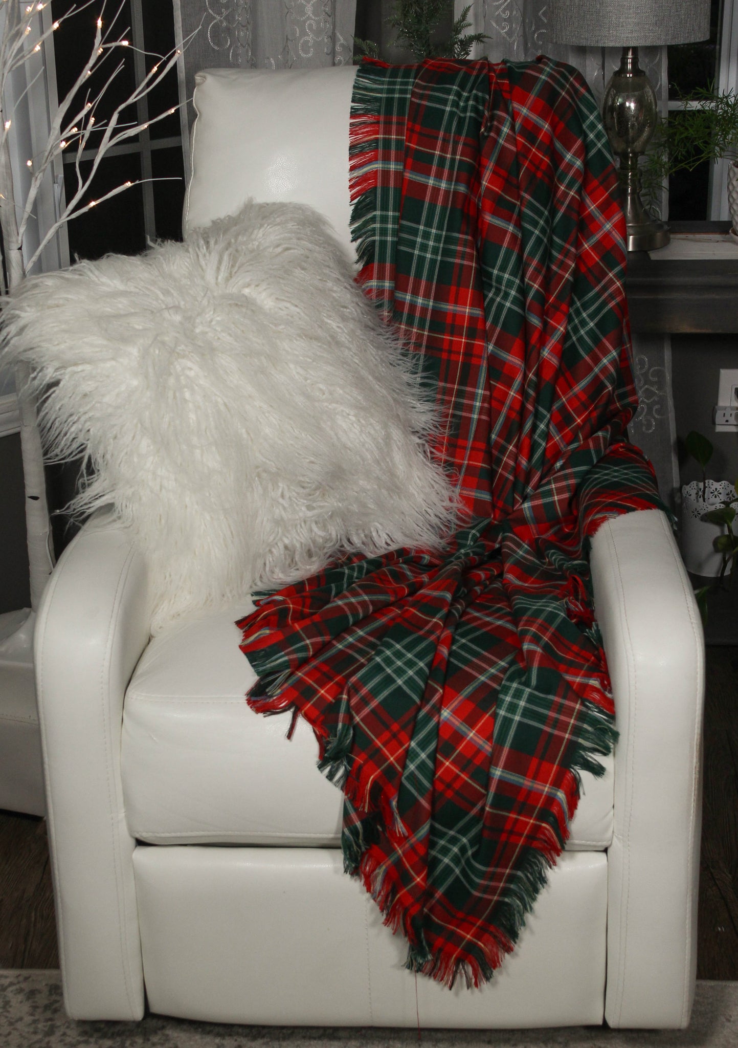 A red and green Christmas plaid New Brunswick tartan throw draped over a white chair with a white pillow, set against a cozy room background.
