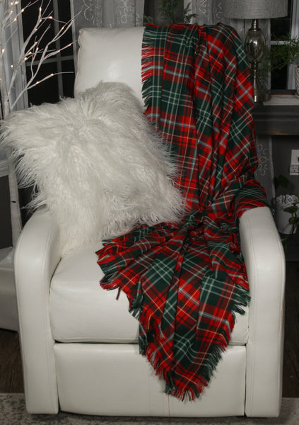A red and green Christmas plaid New Brunswick tartan throw draped over a white chair with a white pillow, set against a cozy room background.