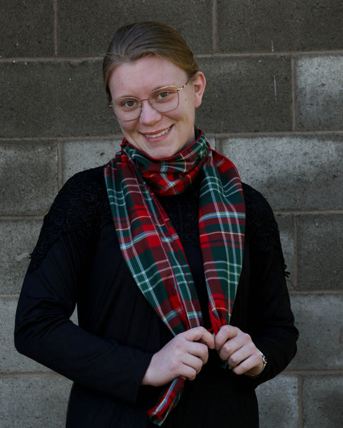 Woman wearing a red and green plaid scarf against a brick wall