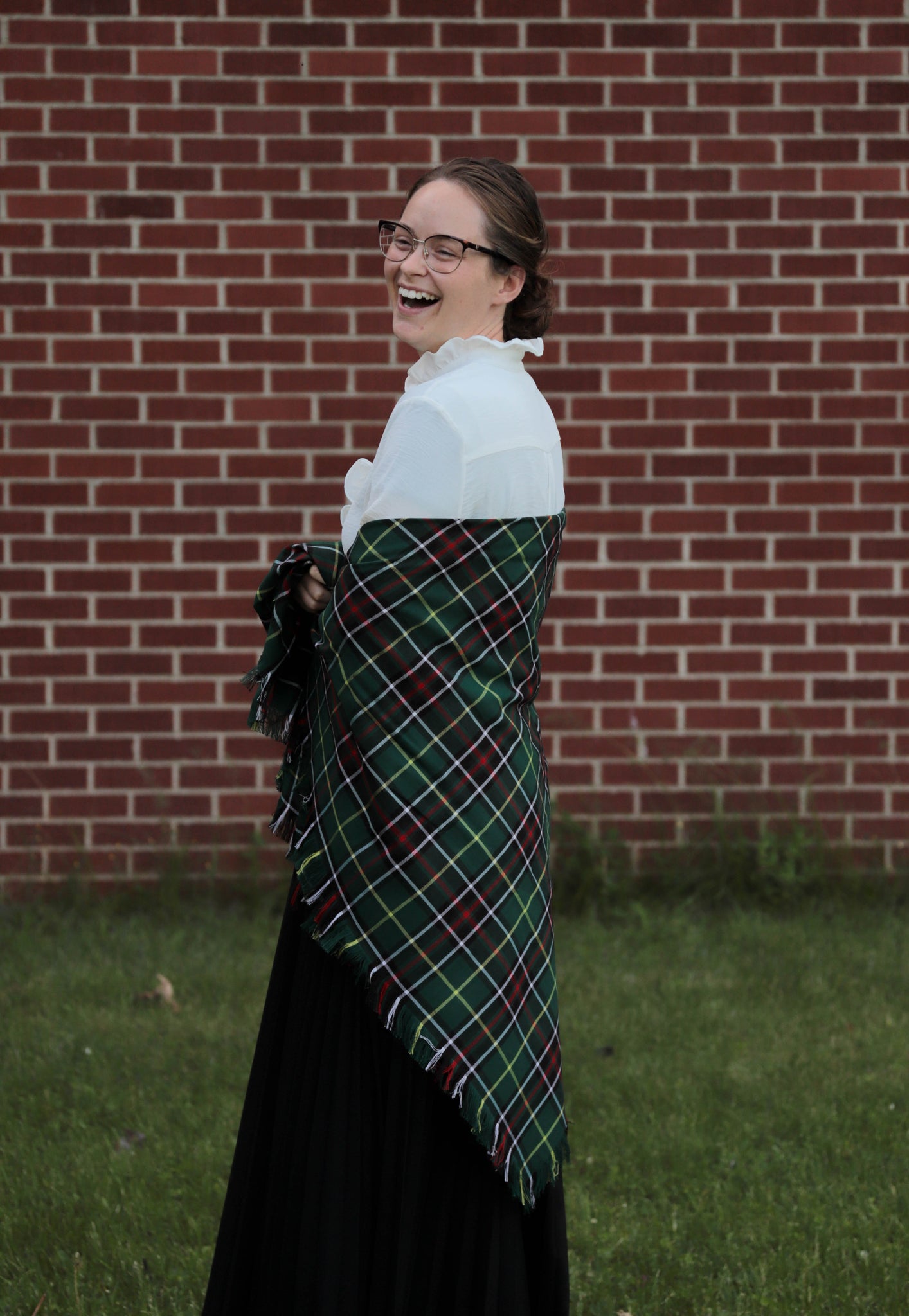 Laughing woman wearing a green plaid Newfoundland tartan blanket scarf shawl in front of a brick wall