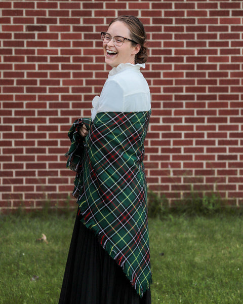 Woman wearing a green plaid Newfoundland tartan shawl in front of a brick wall