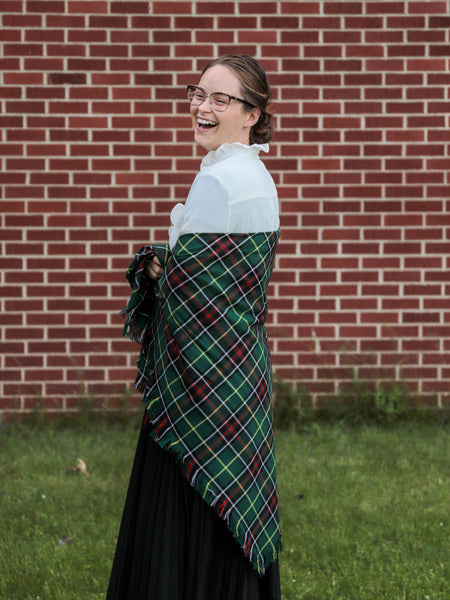 Woman wearing a green plaid shawl in front of a brick wall