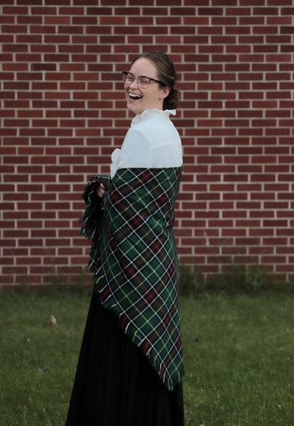 Laughing woman wearing a green plaid Newfoundland tartan blanket scarf shawl in front of a brick wall