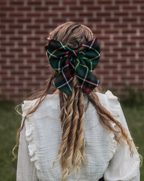 Person with long hair tied back with a  Newfoundland tartan green plaid bow against a brick wall.