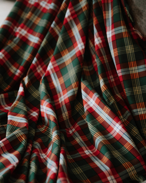 A close-up of Northwest Territories tartan plaid fabric with a classic tartan pattern in green, red, white, and yellow.