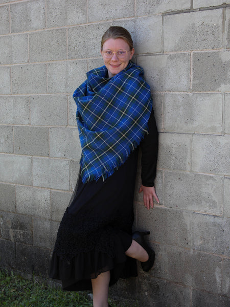 Person wearing a blue plaid shawl against a gray brick wall