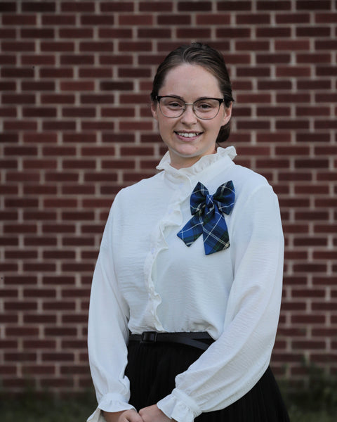 woman wearing a white blouse with a blue plaid bow against a brick wall