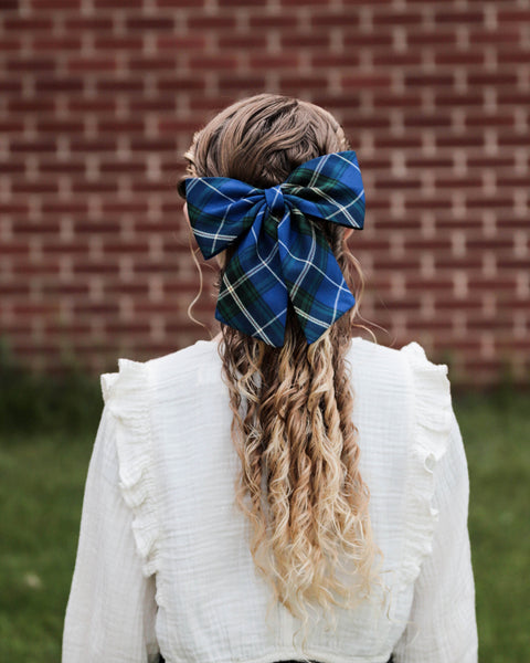 Girl with plaid hairbow and white sweater with long blond curls against a brick wall