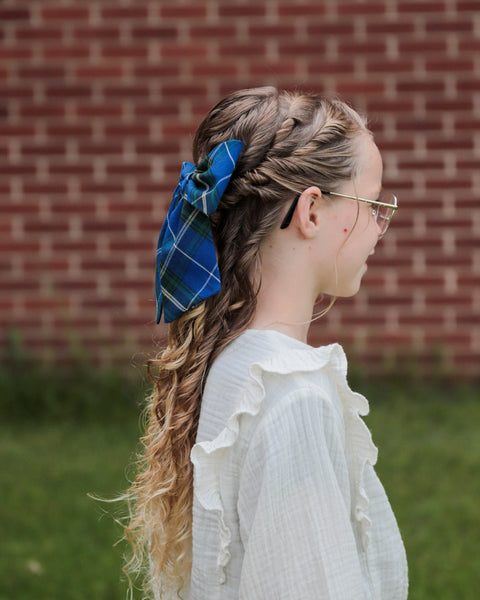 Person with braided hair and blue plaid hair bow in front of a brick wall