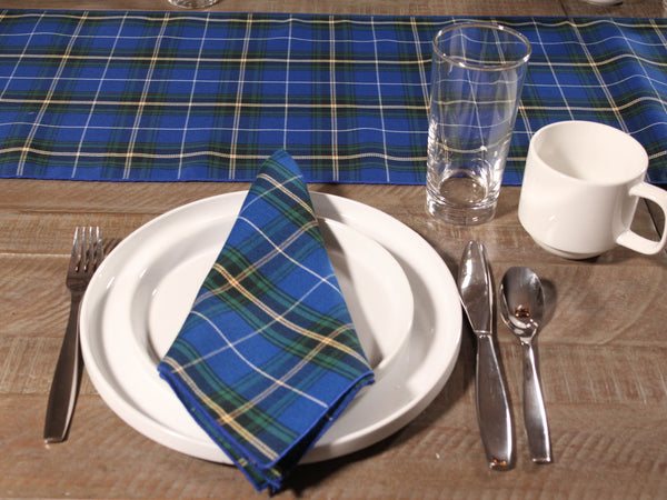 Royal Blue Plaid napkin on a white plate with cutlery and a glass, and table runner made in Canada on a wooden table.