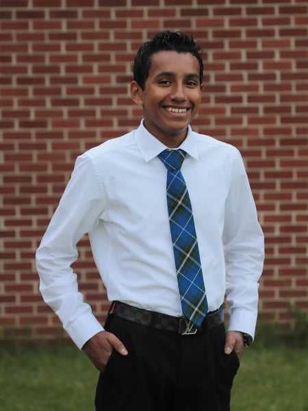 Man wearing a white shirt and blue plaid tie standing in front of a brick wall.