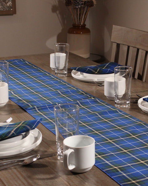 Dining table set with blue checkered table runner, white plates, cups, and glasses.