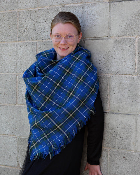 Person wearing a blue plaid shawl against a concrete wall