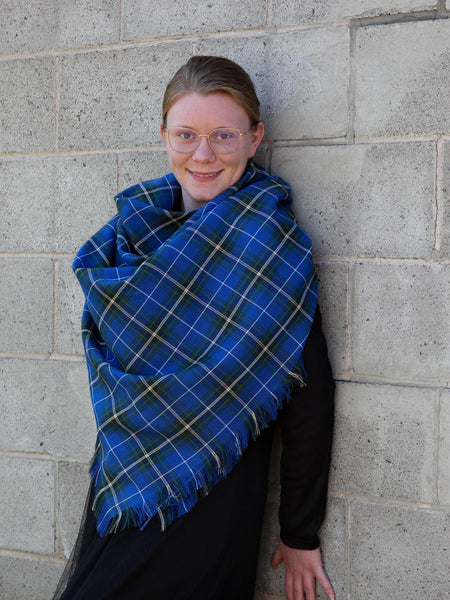 Person wearing a blue plaid Nova Scotia tartan scarf against a gray brick wall