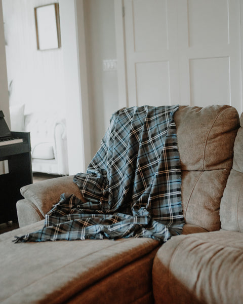 A blue and gray plaid Nunavet tartan  throw blanket draped over a beige fabric sofa in a bright, modern living room.