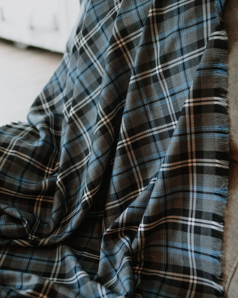 A close-up of a plaid Nunavet tartan throw blanket draped over a chair, featuring a pattern of dark gray, black, light blue, and white stripes.