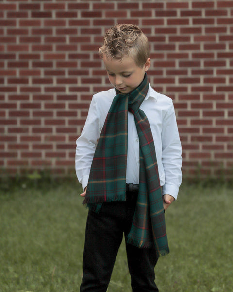Child looking down at graass, wearing an Ontario tartan plaid scarf in front of a brick wall. Made by Taylors Tartans