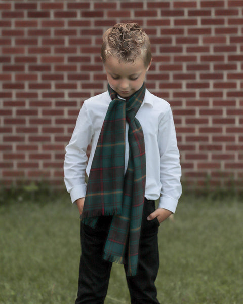 Child wearing a teal and brown plaid scarf over a white shirt in front of a brick wall