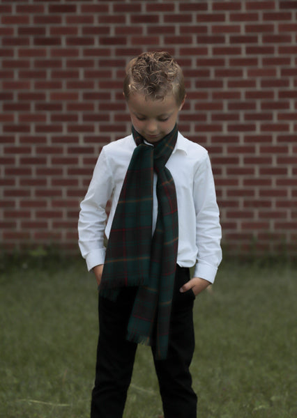 Child wearing a white shirt, black pants, and a dark plaid scarf in front of a brick wall.