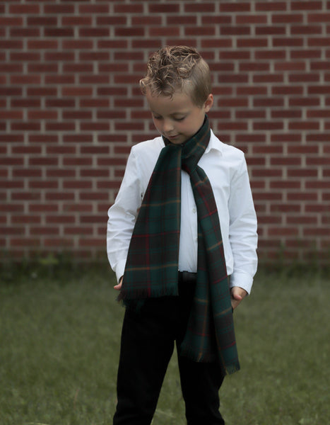 Boy wearing white shirt and green plaid scarf against a brick wall