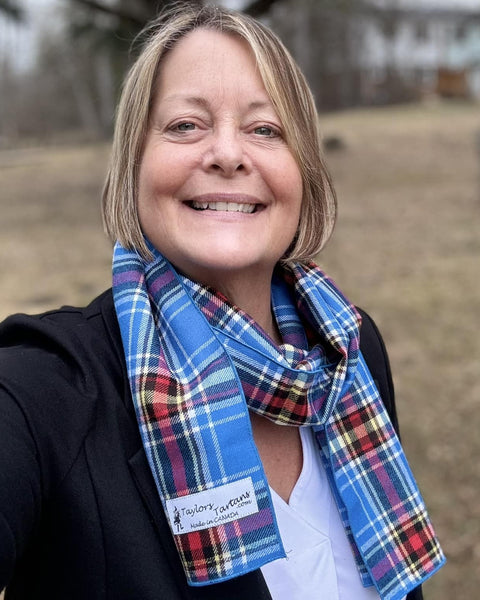 Woman wearing a blue plaid scarf with a visible Taylors Tartans brand label outdoors.