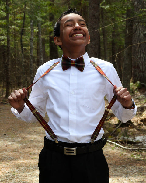 Laughing youth pulling at his suspenders and a bow tie in a forest setting