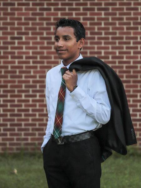 Young man in formal attire with a PEI tartan tie and jacket over his shoulder against a brick wall.