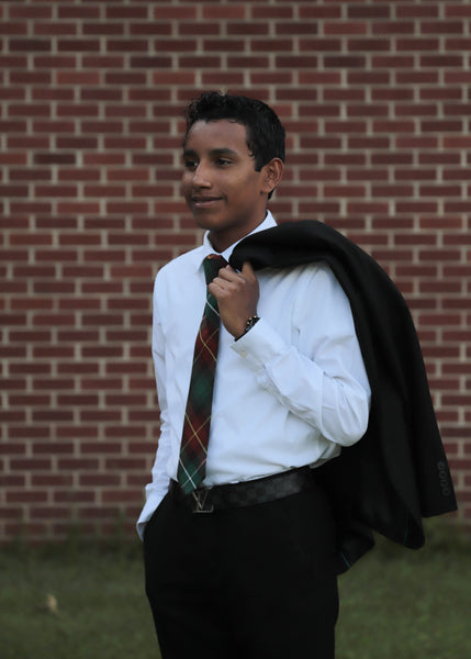 Young man wearing a green, gold, red and white plaid necktie and a white shirt with a black jacket hung over his shoulder.