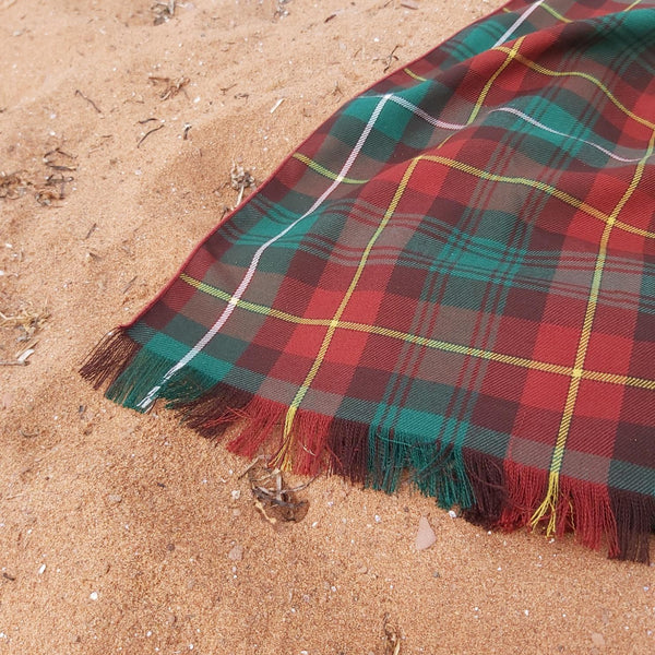 Close-up of plaid scarf with red, green, and yellow colors laid out on a sandy beach.