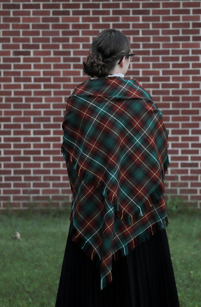 Woman wearing a PEI tartan blanket shawl with her back to the camera, facing a brick wall.