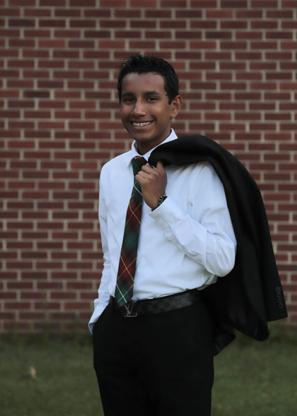 Young man wearing a Prince Edward Island tartan plaid necktie with a white shirt and black jacket standing against a red brick wall.