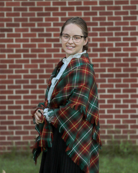 Person wearing a PEI tartan plaid shawl in front of a brick wall