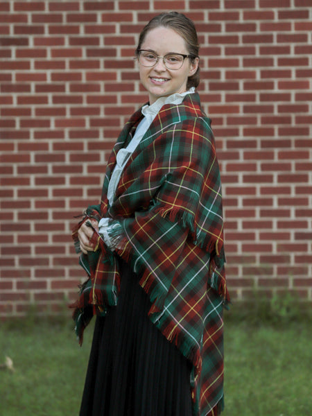 Person wearing a green, light orange, and brown plaid shawl in front of a brick wall
