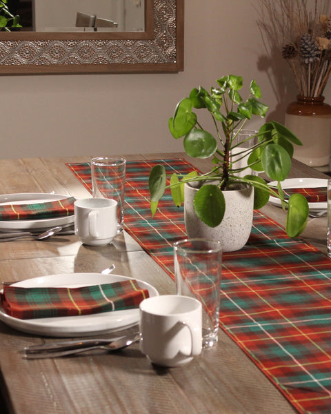 Dining table set with a rust green white and teal plaid tablecloth, cups, plates, and a plant.