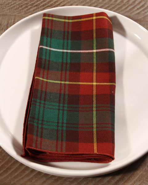 Folded brown and green plaid napkin on a white plate with on a wooden table