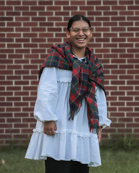 Person wearing a white dress and Quebec tartan plaid scarf in front of a brick wall