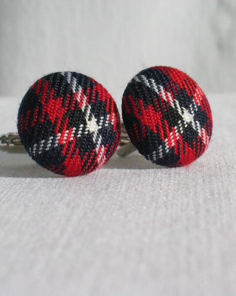 Pair of round red, navy, and white plaid cuff links on a light gray background