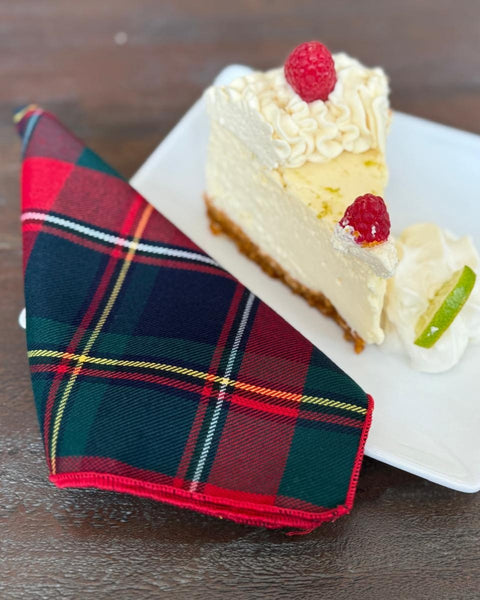 Slice of cheesecake with raspberries on a white plate, accompanied by a Quebec plaid napkin.