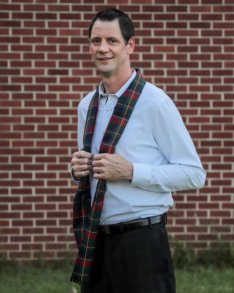 Man wearing a navy and red plaid Quebec scarf in front of a brick wall